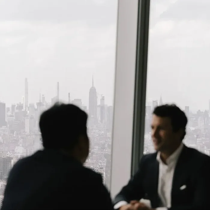 Two colleagues in conversation in a high-rise office overlooking the city